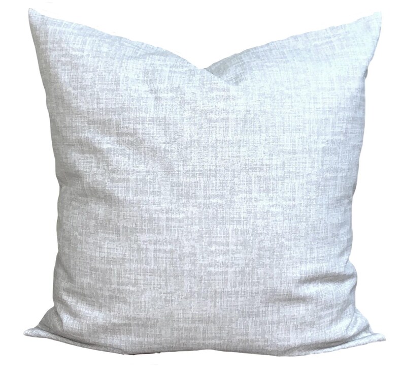 May include: A square, light grey decorative cushion with a textured fabric. The cushion has a neutral colour and a simple design, suitable for various home decor styles. The cushion is approximately 50 cm square.