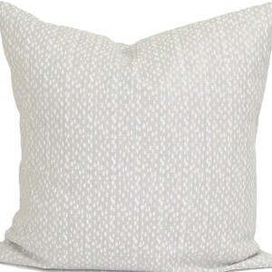 May include: A square cushion with a light grey backdrop and a pattern of small white dots. The cushion has a soft, textured appearance, suitable for home decor.
