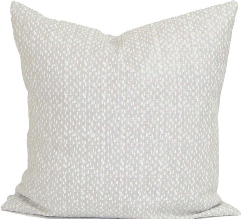 May include: A square cushion with a light grey backdrop and a pattern of small white dots. The cushion has a soft, textured appearance, suitable for home decor.