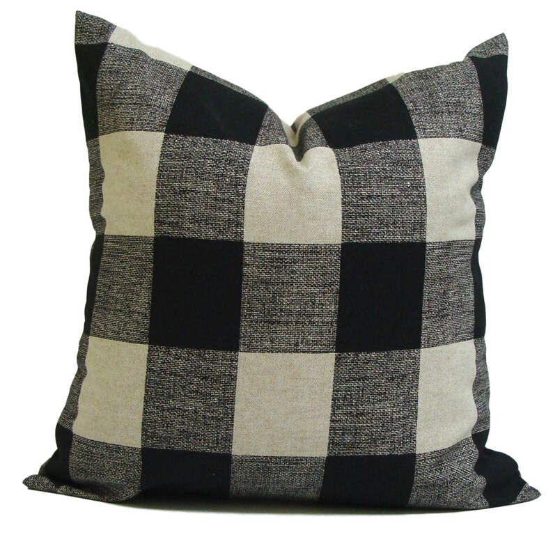 K&ouml;nnte beinhalten: Quadratisches Zierkissen mit einem schwarz-beigen B&uuml;ffelkaromuster. Das Kissen hat eine strukturierte Oberfl&auml;che und ein weiches Aussehen. Es ist f&uuml;r den dekorativen Einsatz auf einem Bett oder Sofa geeignet.