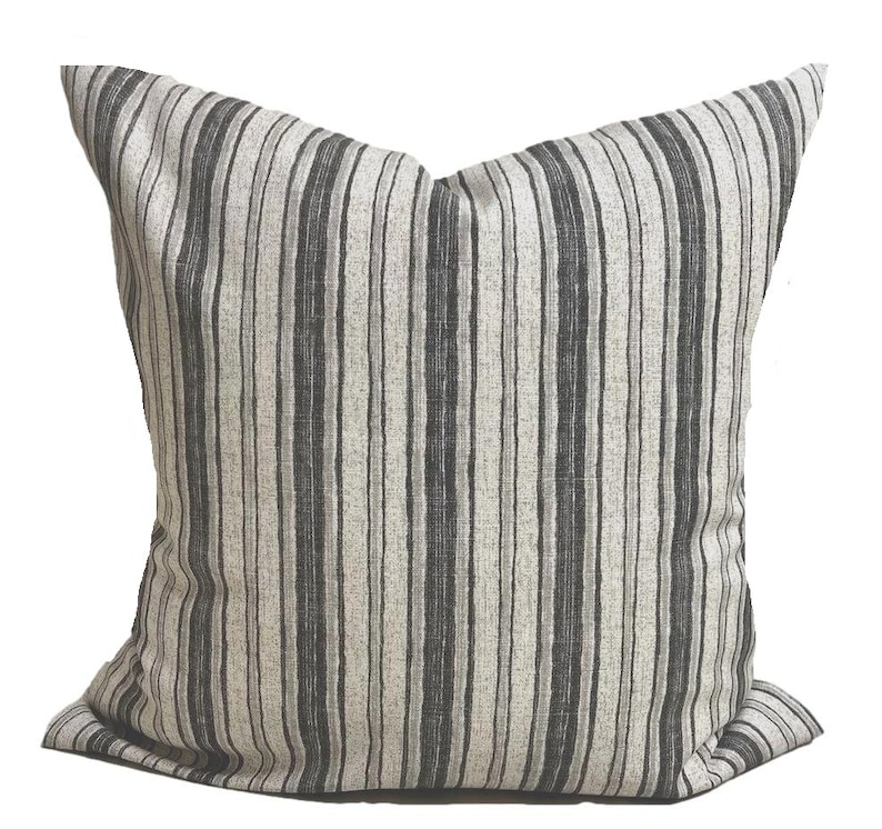 May include: Square decorative pillow with vertical stripes in shades of gray and off-white. The pillow has a soft, textured appearance and a classic design, suitable for home decor.