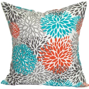 May include: Square throw pillow with a white background and a floral pattern. The flowers are in shades of gray, teal, and orange. The pillow is a decorative accent for a sofa or bed.