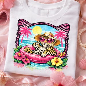 May include: White t-shirt featuring a cartoon leopard wearing sunglasses and a straw hat, relaxing in a pink inflatable ring. The design includes a beach scene with palm trees, flowers, and a sunny sky. The leopard has a spotted coat.