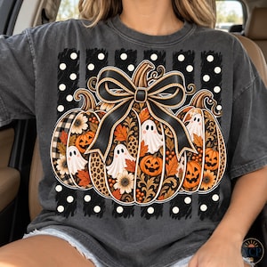 May include: A charcoal gray t-shirt featuring a graphic of three pumpkins adorned with a large black bow. The design includes white ghosts, orange jack-o'-lanterns, sunflowers, autumn leaves, and leopard print patterns set against a black and white polka dot background.
