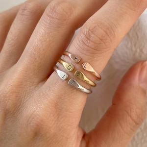 May include: Three open-ended rings in rose gold, yellow gold, and silver tones. Each ring features two flat, rounded ends, with the letters K and L on the rose gold ring, Q and E on the yellow gold ring, and J and T on the silver ring.