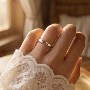 Peut inclure: Une bague ouverte de couleur argentée avec deux extrémités plates, chacune gravée d'une lettre noire. Une extrémité porte la lettre J et l'autre extrémité porte la lettre T. L'anneau présente une finition lisse et polie avec un design ouvert.