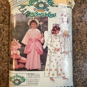 Op de afbeelding: Een Butterick Cabbage Patch Kids naaipatroon-envelop, nummer 3490, met illustraties van kinderen in een roze feeënkostuum en een wit engelenkostuum met sterrenpatroon, vleugels en een halo, inclusief tekst en merknaam.