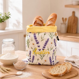 Peut inclure: Un sac à pain en tissu avec un fond crème orné d'un motif floral de lavande violette et de marguerites blanches. Le sac possède une doublure intérieure jaune et le prénom Austin est brodé en fil jaune sur le devant. Deux pains sont à l'intérieur.