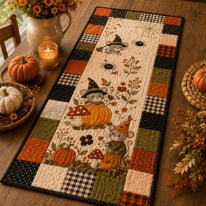 May include: A rectangular quilted table runner featuring a cream-colored center panel with appliqued mice wearing witch hats, pumpkins, mushrooms, and spiders. The border consists of a patchwork pattern in black, orange, and olive green.