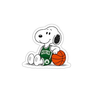 May include: A sticker featuring a white cartoon dog sitting down and wearing a green and white basketball jersey with the word CELTICS and a shamrock logo printed on it. The dog is resting one paw on a round, orange basketball with black lines.
