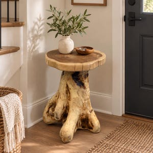 May include: A side table crafted from a natural tree stump with a smooth, circular wooden top featuring visible grain and a light-colored, textured base. A small white ceramic vase with green leaves and a small wooden bowl sit on the surface.