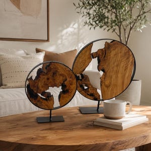 May include: Two circular decorative sculptures featuring natural, irregular-shaped wood slices encased in thin black metal frames. Each sculpture is mounted on a square black metal base, showcasing the raw, textured grain and dark charred edges of the wood.