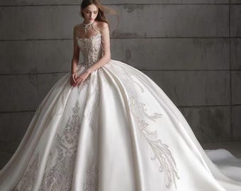 Può includere: Un abito da ballo bianco lungo fino a terra con un corpetto strutturato caratterizzato da intricati ricami e perline argentate. L'abito presenta uno scollo all'americana alto con delicati dettagli a catena sulle spalle e una gonna voluminosa.