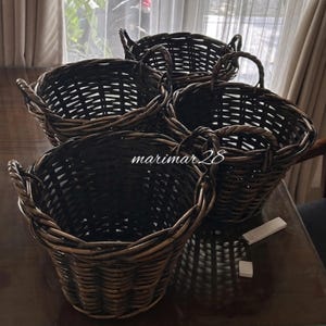 May include: Four woven wicker baskets with handles. The baskets are a dark brown color and have a round shape. The baskets are arranged in a group, with some overlapping. The baskets are suitable for storage or decoration.