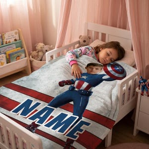 May include: A child's bed with a Captain America-themed blanket. The blanket features a graphic of Captain America with a shield, the word "NAME" in large letters, and red and white stripes. A child is sleeping on the bed.