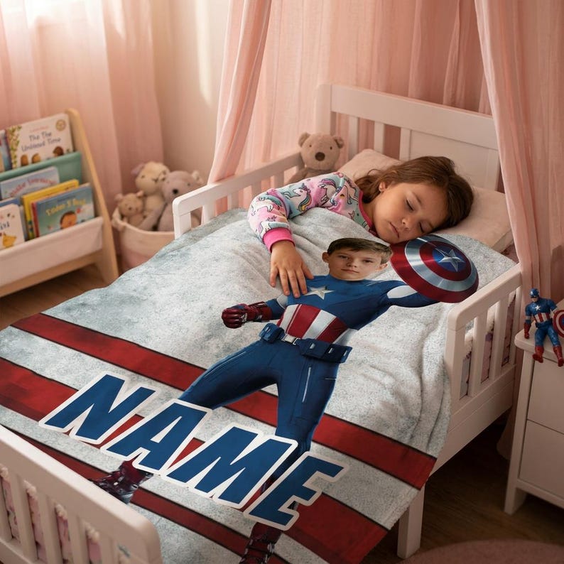 May include: A child's bed with a Captain America-themed blanket. The blanket features a graphic of Captain America with a shield, the word "NAME" in large letters, and red and white stripes. A child is sleeping on the bed.