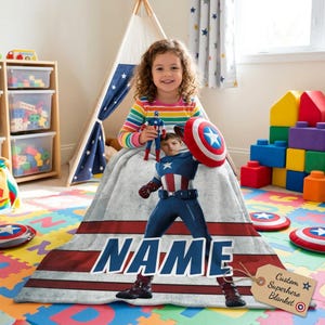 May include: A personalized superhero blanket featuring a Captain America design with the name "NAME" in large blue letters. The blanket has a red and white striped border and includes a tag that says "Custom Superhero Blanket".