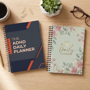 May include: Two spiral-bound daily planners with the text "The ADHD Daily Planner". One planner is navy blue with orange accents, the other is light green with floral designs. A gold pen, coffee cup, glasses, and paper clips are also on the wooden surface.