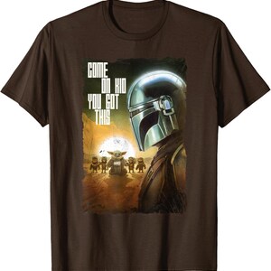 Op de afbeelding: Bruin T-shirt met een afbeelding uit de Star Wars-serie, The Mandalorian. Het ontwerp toont de helm van de Mandalorian, Grogu en de tekst "COME ON KID YOU GOT THIS". De achtergrond toont een woestijnlandschap met een ondergaande zon.