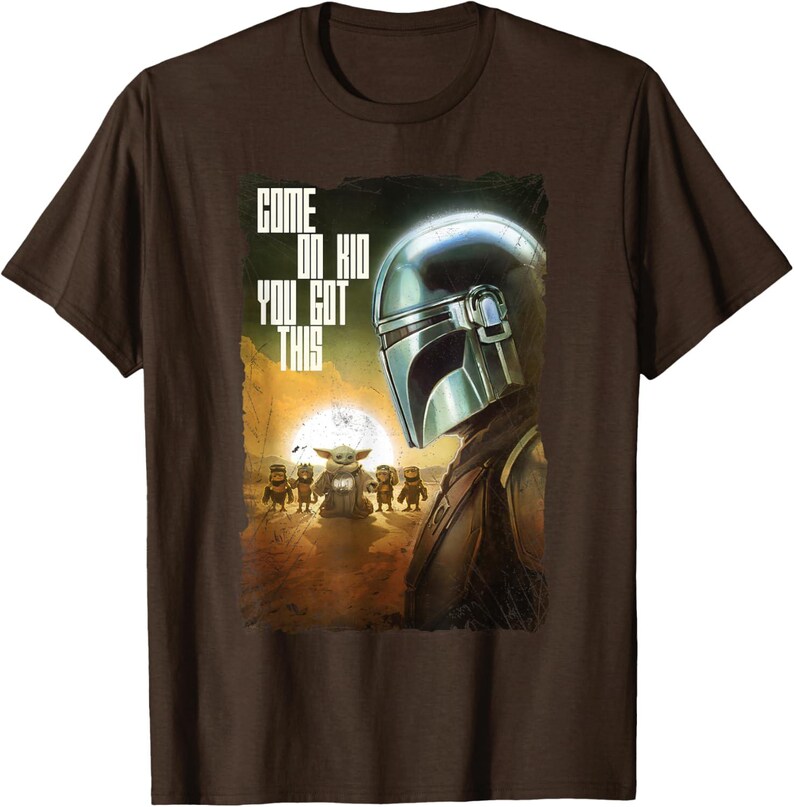 Op de afbeelding: Bruin T-shirt met een afbeelding uit de Star Wars-serie, The Mandalorian. Het ontwerp toont de helm van de Mandalorian, Grogu en de tekst "COME ON KID YOU GOT THIS". De achtergrond toont een woestijnlandschap met een ondergaande zon.