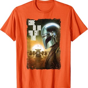 Op de afbeelding: Oranje t-shirt met een afbeelding uit de Star Wars-serie. Het ontwerp toont de helm van de Mandalorian, Grogu en andere personages, met de tekst "COME ON KID YOU GOT THIS".
