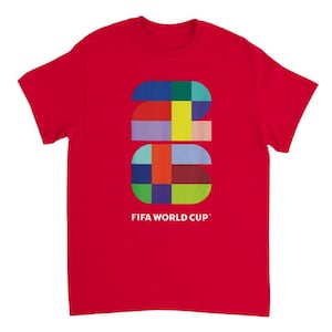 May include: A bright red short-sleeve t-shirt featuring a large, colorful graphic of the number 2026 composed of various geometric shapes in blue, yellow, green, and pink. Below the graphic, the text FIFA WORLD CUP is printed in white.