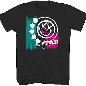 May include: A black short-sleeve t-shirt featuring a graphic print of a white smiley face with X-shaped eyes, surrounded by a circular arrow design. The graphic includes teal and pink brushstroke accents and the text blink-182 in white.