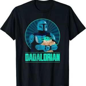 以下が含まれることがあります： 黒いTシャツ。マンダロリアンがグローグーを抱きかかえる、ターコイズと青のグラフィック。テキスト「DADALORIAN」はターコイズ色。デザインは放射線状のラインが入った青い円を背景にしている。