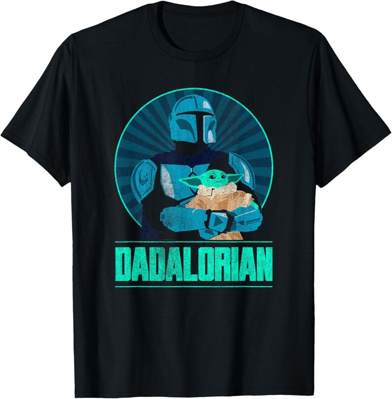 以下が含まれることがあります： 黒いTシャツ。マンダロリアンがグローグーを抱きかかえる、ターコイズと青のグラフィック。テキスト「DADALORIAN」はターコイズ色。デザインは放射線状のラインが入った青い円を背景にしている。