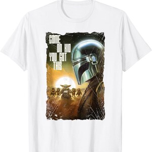 Op de afbeelding: Wit T-shirt met een afbeelding uit de Star Wars-serie. Het ontwerp toont de Mandalorian, Grogu en andere personages, met de tekst "COME ON KID YOU GOT THIS". De achtergrond is een zonsondergang.