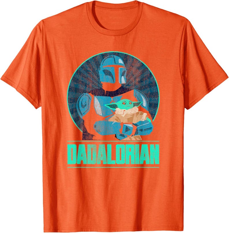 以下が含まれることがあります： オレンジ色のTシャツ。青い円の中に、マンダロリアンキャラクターがグローグーキャラクターを抱いているグラフィック。テキスト「DADALORIAN」はターコイズ色で下に印刷されています。