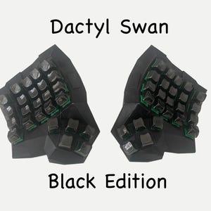 May include: A black Dactyl Swan Black Edition split ergonomic keyboard featuring a contoured, multi-faceted geometric case design with black keycaps and visible green switch stems beneath the keys, arranged in two separate halves.