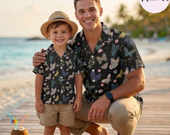 Peut inclure: Un ensemble assorti de chemises à manches courtes boutonnées avec un fond noir et un motif de papillons colorés. L'enfant porte un short beige et un chapeau de paille, tandis que l'adulte porte un pantalon beige et des lunettes. Logo Hippydenmark.