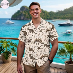 May include: A short-sleeved button-down shirt in a light cream color featuring a repeating brown ink illustration pattern of various dinosaur skeletons, including Tyrannosaurus Rex, Stegosaurus, and Pterodactyl, with printed text labels.