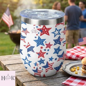 May include: A white stainless steel tumbler with a clear lid, featuring a repeating pattern of red, white, and blue stars, some of which contain American flag stripes. The tumbler has a metallic rim and a smooth, cylindrical body design.