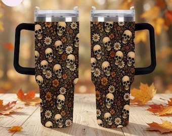 Peut inclure: Deux gobelets en acier inoxydable avec poignées noires et couvercles transparents, arborant un motif répétitif de crânes humains beiges entremêlés de fleurs orange et blanches sur fond brun foncé, présentés côte à côte sur une surface en bois.