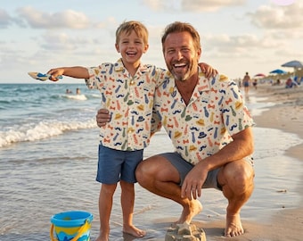 Peut inclure: Deux chemises assorties à manches courtes et boutonnées, présentant un fond crème avec un motif répétitif coloré de cravates, nœuds papillon, moustaches, chapeaux et lunettes. Les chemises ont un col classique et sont portées avec un short bleu.