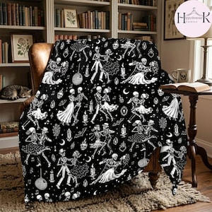 May include: A black throw blanket featuring a repeating white pattern of skeletons dancing in formal attire. The design includes disco balls, candles, bats, and musical notes scattered across the fabric, creating a detailed monochromatic scene.