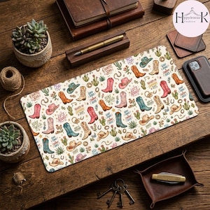 May include: A rectangular desk mat featuring a repeating pattern of colorful cowboy boots, cacti, and horseshoes on a cream background. The design includes scattered text phrases like Let's Rodeo, Stay Wild, and Country Soul in various fonts.