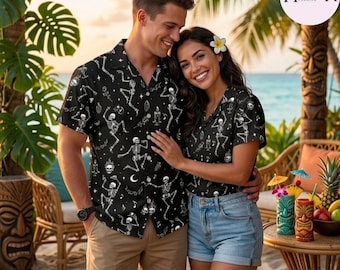 Peut inclure: Deux chemises à manches courtes boutonnées avec un fond noir et un motif répétitif blanc de squelettes dansants, de croissants de lune et d'étoiles. Les chemises ont un col classique et une fermeture boutonnée, portées avec un short.