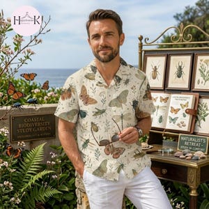 May include: A short-sleeved button-down shirt in an off-white color featuring an all-over print of various insects, butterflies, and botanical elements. The shirt has a classic collar and is paired with plain white trousers.