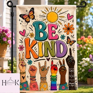 May include: A beige garden flag with the words "BE KIND" in colorful, bubble letters. The flag features illustrations of hands making various hand gestures, butterflies, flowers, hearts, and a sun.