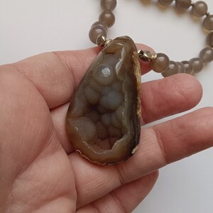 May include: A brown and gray agate pendant necklace with a teardrop-shaped pendant. The pendant has a unique pattern of white and gray agate.