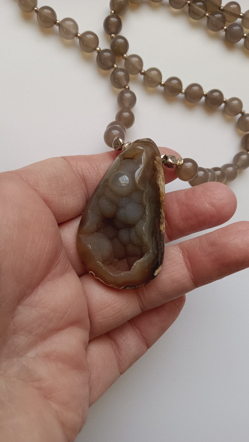 May include: A brown and gray agate pendant necklace with a teardrop-shaped pendant. The pendant has a unique pattern of white and gray agate.
