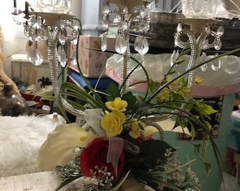 May include: White metal candelabra with three crystal candle holders and a floral arrangement of white calla lilies, yellow roses, and green foliage.