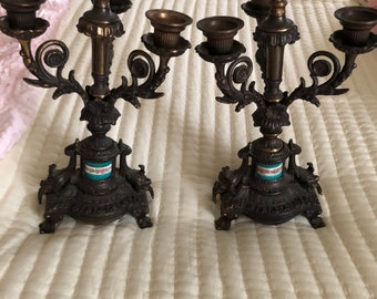 May include: A pair of ornate bronze candle holders with three arms each. The candle holders have a decorative design with a blue and white porcelain base.