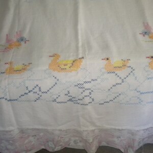 May include: White cotton tablecloth with embroidered ducks and birds in yellow, blue, pink, and green. The tablecloth has a lace trim.