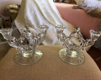 May include: A pair of clear glass candle holders with ornate designs. Each holder has three candle cups and a wide base.