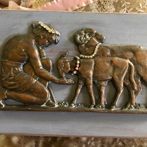 May include: A bronze sculpture of a woman kneeling and reaching out to two lambs. The woman is wearing a crown of rhinestones and the lambs are wearing rhinestone collars.