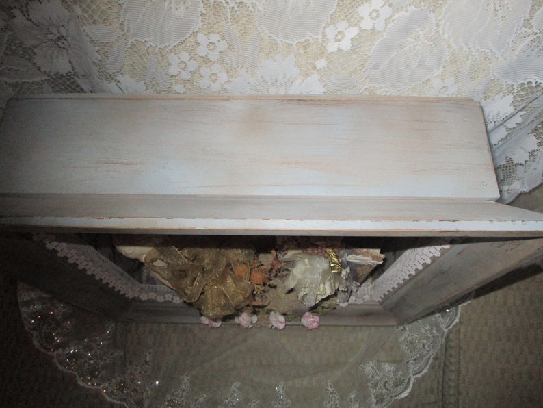 May include: A white wooden box with a distressed finish. The box is open and filled with lace, ribbon, and other decorative items.